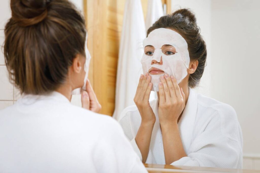 mascarilla facial tipo sábana de un solo uso mujer aplicándosela en el baño